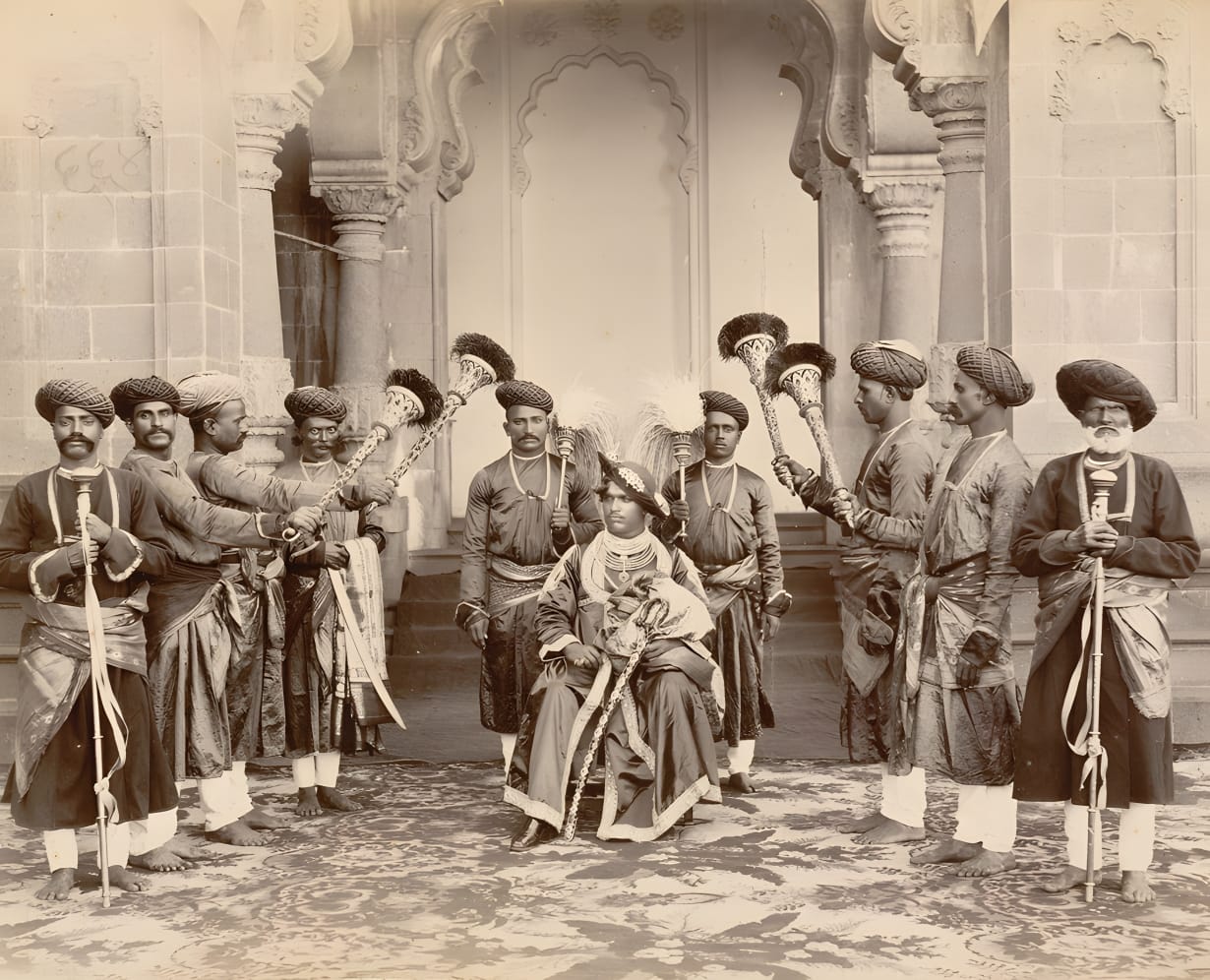 अपने सेवक कर्मचारियों के साथ कुर्सी में बैठे शाहू महाराज की महल के बाहर की तस्वीर